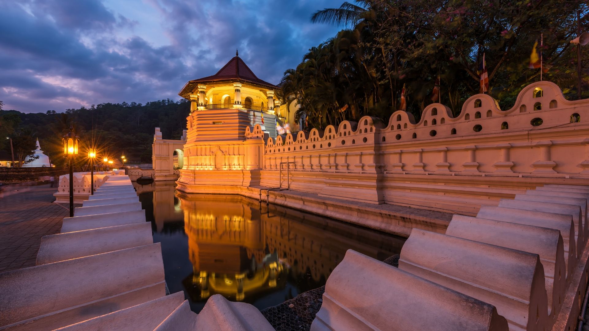 An illuminated temple building with a tiered roof beside a reflecting moat, photographed at dusk.
