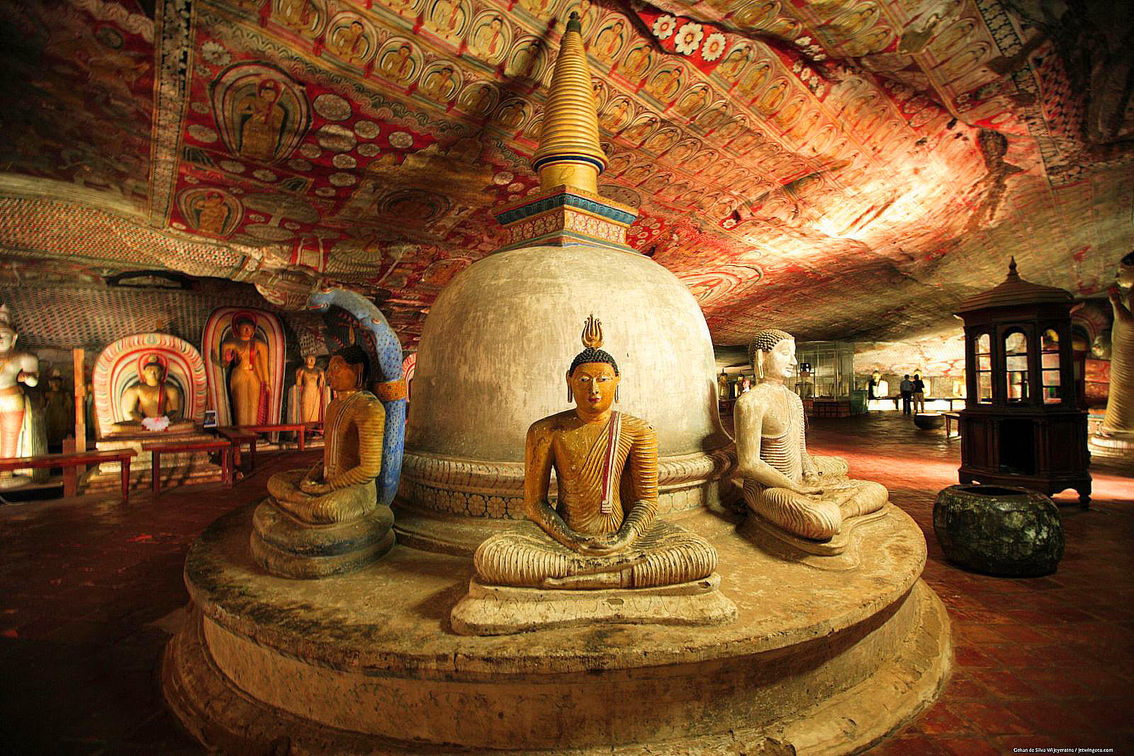 Interior of a painted rock-cave Buddhist temple with seated Buddha statues arranged around a small stupa.