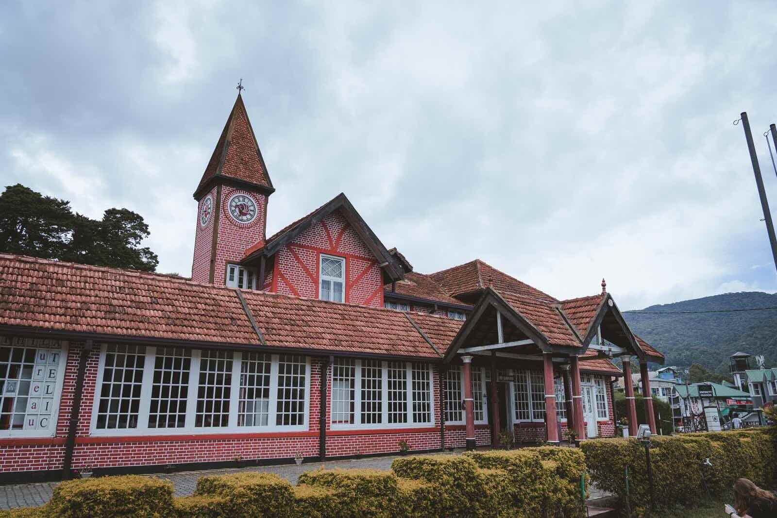 A red-brick colonial-era building with a pointed clock tower, in a Tudor architectural style.