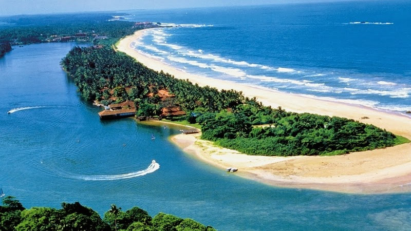 Aerial view of a river mouth meeting the ocean beside a sandy, palm-covered peninsula and a beachfront resort.