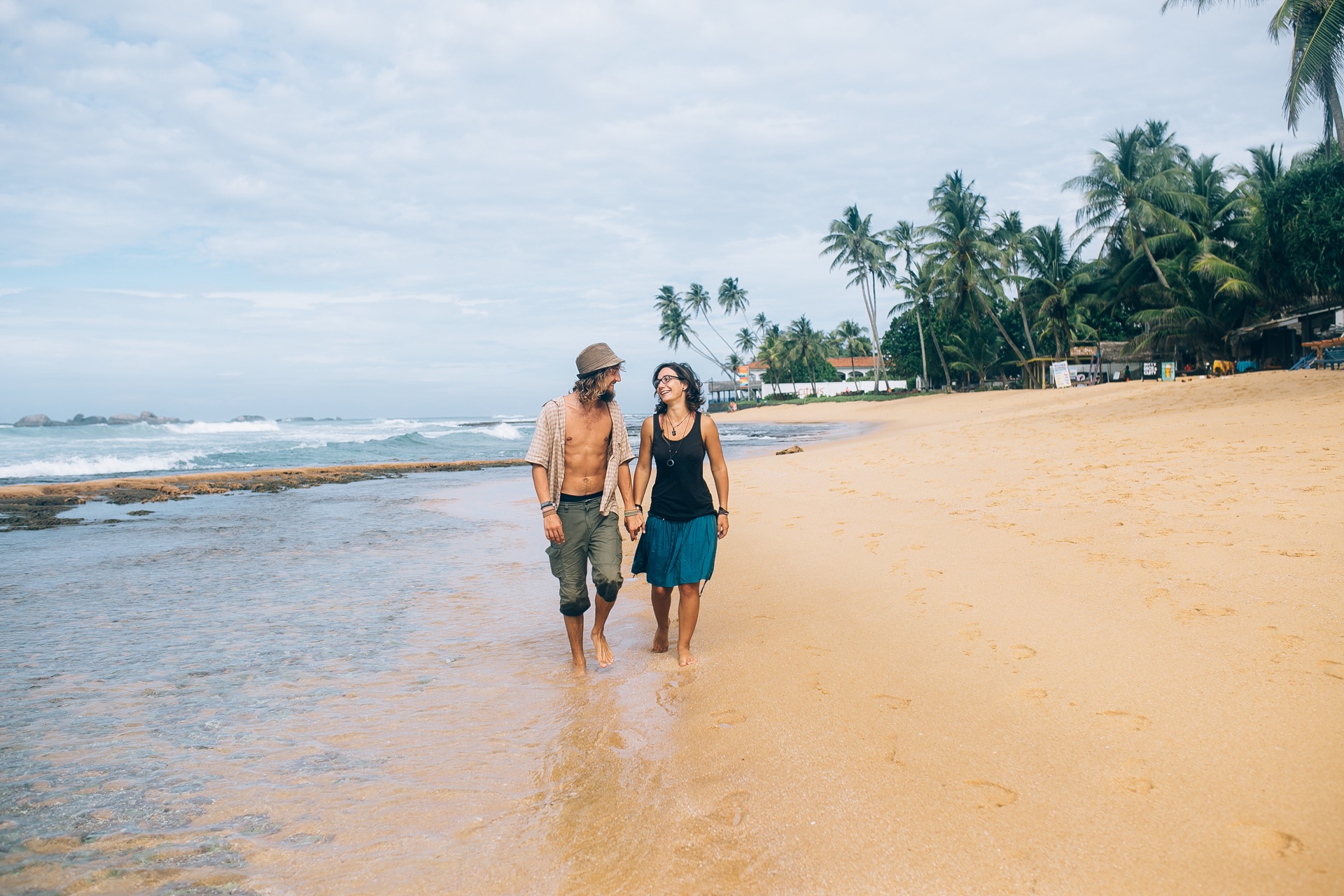A couple walking hand in hand along a beach at dusk.